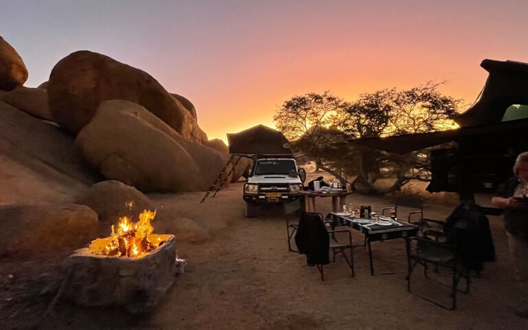 Alt: Lagerfeuer und Safari-Ausrüstung im afrikanischen Wüstenpark bei Sonnenuntergang.
