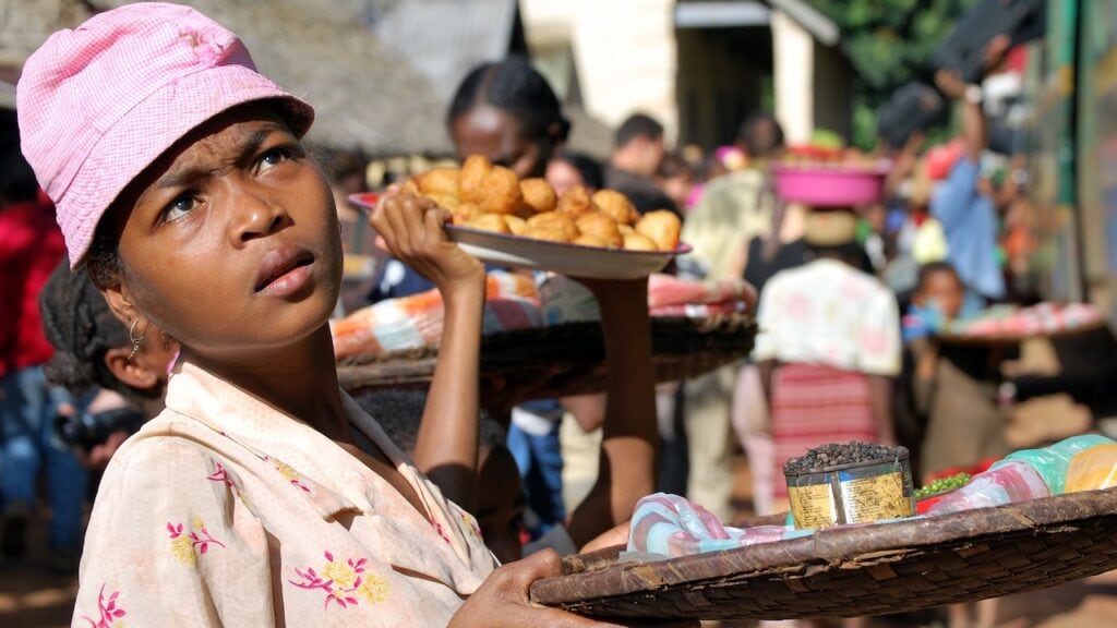 Junge afrikanische Marktfrau verkauft street food bei einem lebhaften Markt in Afrika.