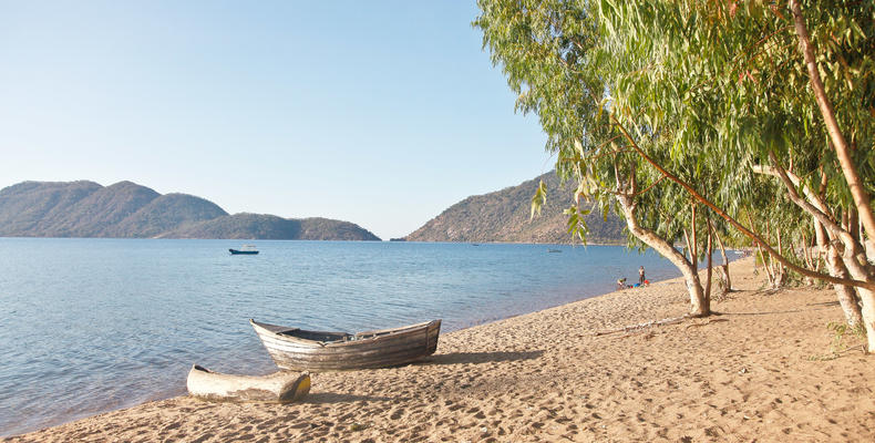 Entspannter Strand an einem afrikansichen See mit Booten und Bergen im Hintergrund, ideal für Urlaub & Naturerlebnis.
