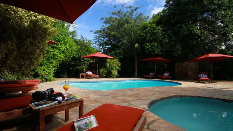 Entspannter Swimmingpool in afrikanischer Lodge mit Sonnenschirmen, ideal für Afrika Urlaub.