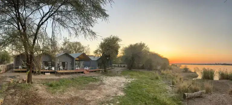 Gemütliche Safari Lodge am Fluss in Afrika bei Sonnenuntergang.