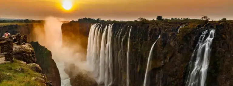 Stimmungsvoller Sonnenuntergang über den Victoriafällen in Afrika mit Wasserfällen, Afrika-Reise, Naturwunder, Touristen, Landschaft.
