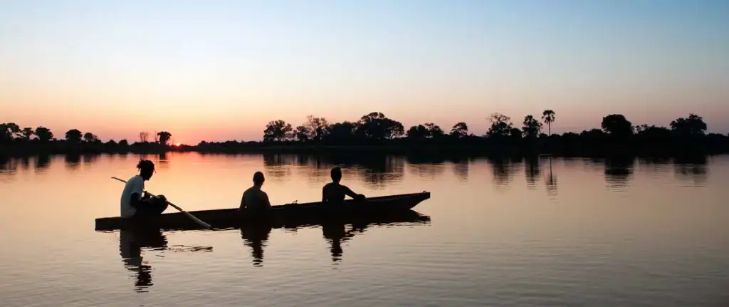 Boot mit drei Personen bei Sonnenuntergang in Afrika, Fluss, Natur, Tourismus.