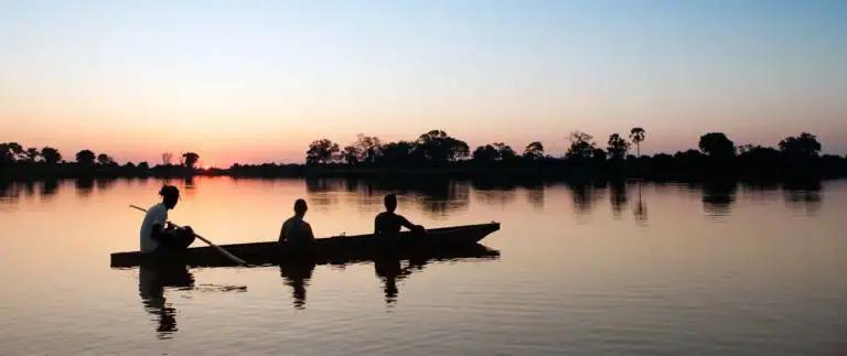 Boot mit drei Personen bei Sonnenuntergang in Afrika, Fluss, Natur, Tourismus.