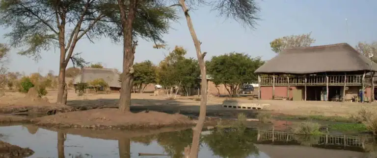 Traditionelle afrikanische Hütten in einer ländlichen Landschaft mit Wasser und Bäumen.