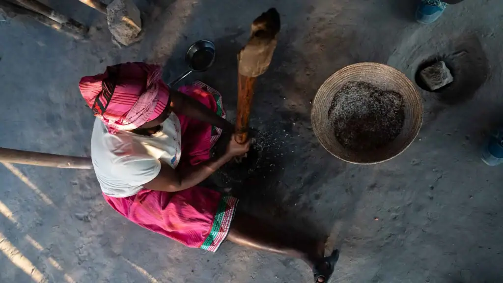 Alt Text: Afrikanischer Handwerker bearbeitet Stein mit Hammer und Meißel im ländlichen Afrika.