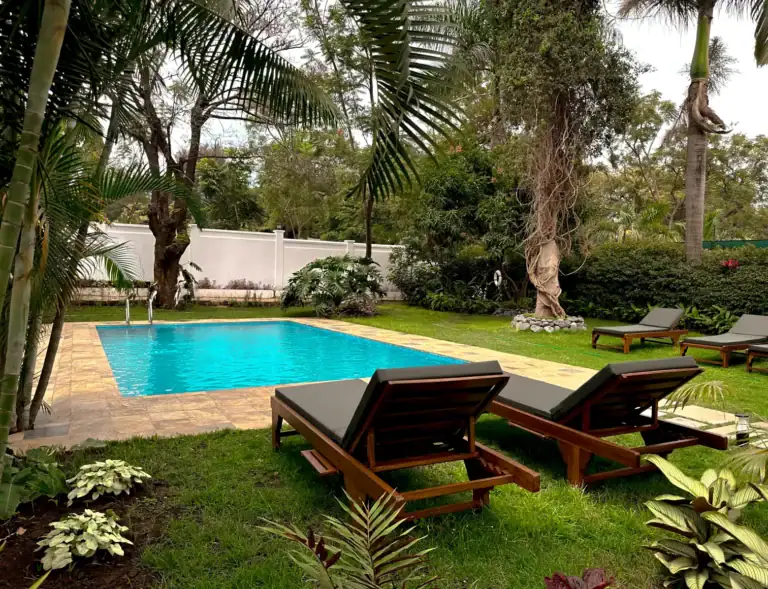 Bunter Pool im tropischen Garten mit Liegestühlen und Palmen.