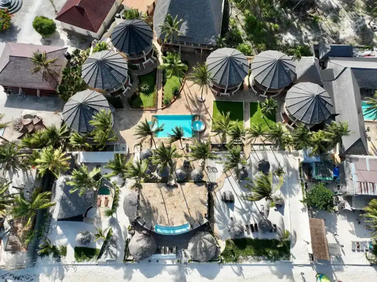 Aerialaufnahme eines afrikanischen Luxushotels mit Pool, Palmen und Strohdächern, ideal für Afrika Safari und Strandurlaub.