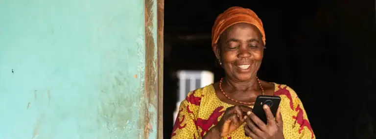 Lächelnde afrikanische Frau benutzt Handy, authentisches Afrika-Reiseerlebnis, lokale Kultur, Digitales Afrika.