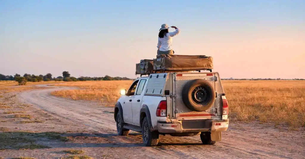 Alt-Text: Frau auf Geländefahrzeug in afrikanischer Savanne bei Sonnenuntergang.