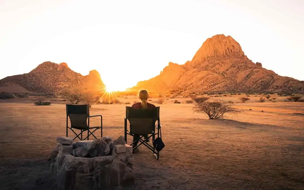 Frau sitzt bei Sonnenuntergang in Namibia-Wüste, Blick auf Felsformationen.