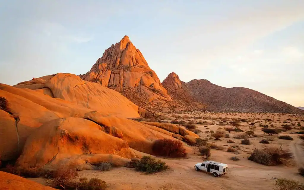 Berglandschaft in Namibia mit orangefarbenen Felsen und Dachzelt im Wüstensand.