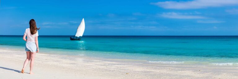 Frau am weißen Sandstrand mit Blick auf das Meer und Segelboot.