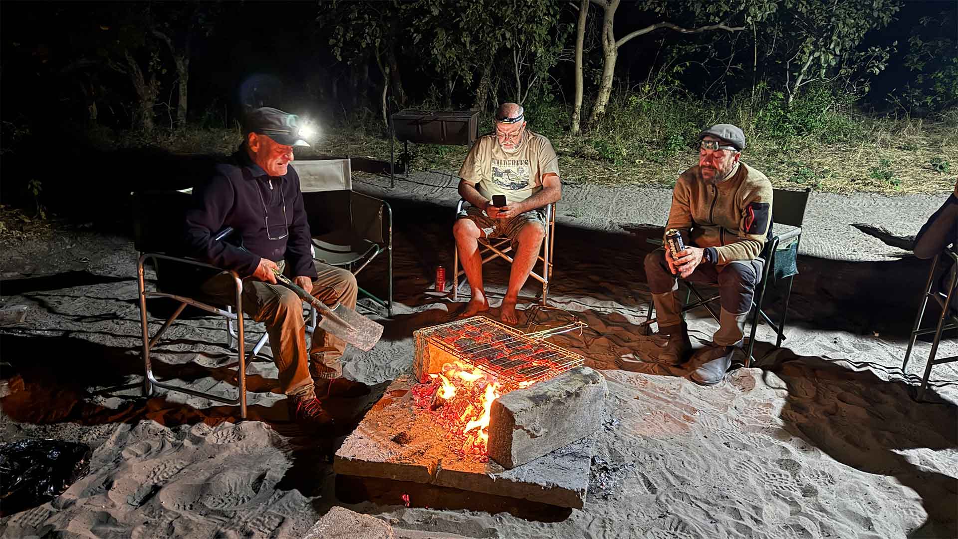Menschen sitzen am Lagerfeuer in der Nacht, Afrika Safari Erlebnis.
