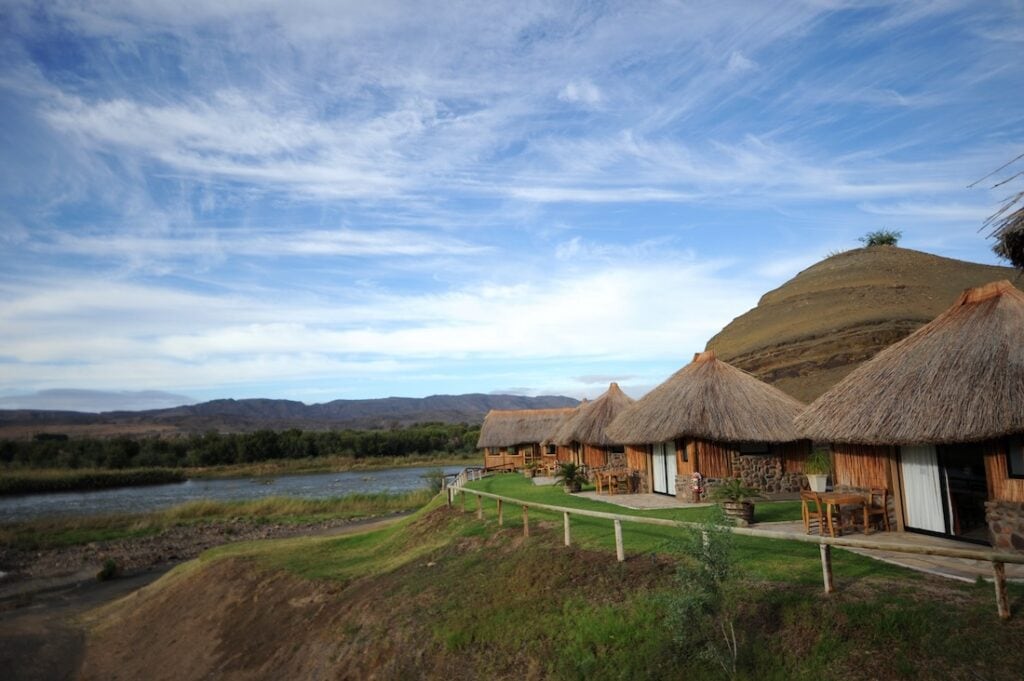 Afrikanische Lodge am Fluss mit Hügeln im Hintergrund, Namibia Reise.