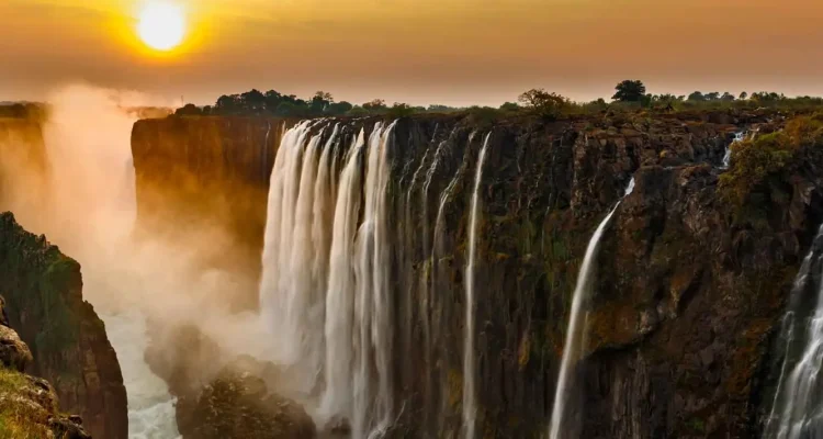 Stimmungsvoller Sonnenuntergang über den Victoriafällen in Afrika mit Wasserfällen, Afrika-Reise, Naturwunder, Touristen, Landschaft.