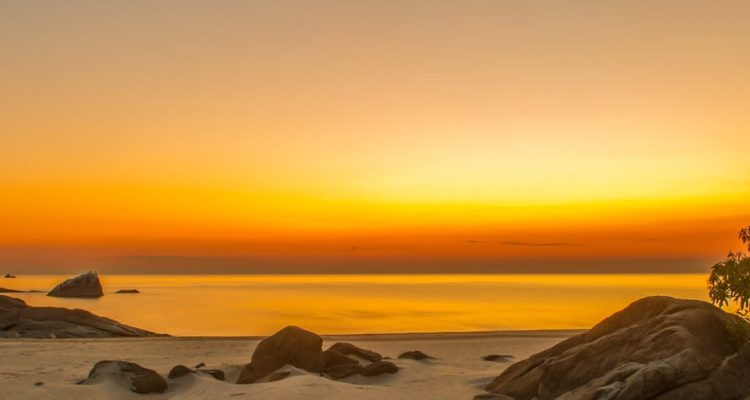 Alt: Malerischer Sonnenuntergang am afrikanischen Strand mit Felsen und Palmen.