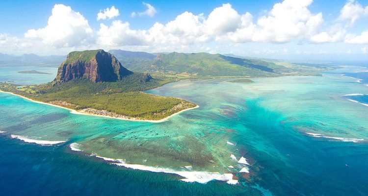 Aerial shot of a tropical island with turquoise waters, palmstrände, und grüne Berge in Afrika.