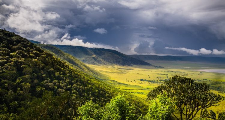 Blick auf den Ngorongoro-Krater mit grünen Bergen und dunklen Wolken, Afrikas Tierparadies.