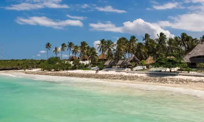 Strand mit Palmen, Tiki-Hütten, türkisblauem Wasser, Sonnenuntergang, exotisches Afrika-Reiseparadies.