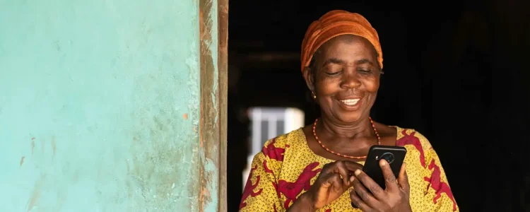 Lächelnde afrikanische Frau benutzt Handy, authentisches Afrika-Reiseerlebnis, lokale Kultur, Digitales Afrika.