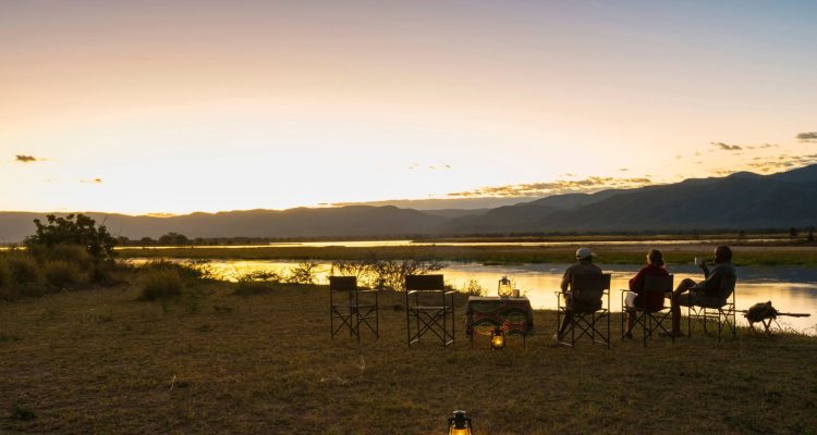 Menschen genießen Sonnenuntergang am Fluss in Afrika, Safari, Wildtiere, Naturerlebnis in Afrika.